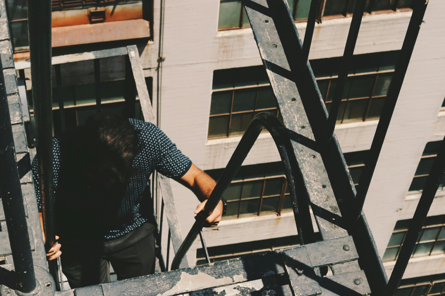 A person climbing a metal fire escape ladder on the exterior of a building.