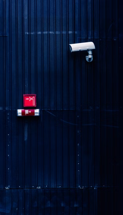 White CCTV security camera mounted beside a building alarm system